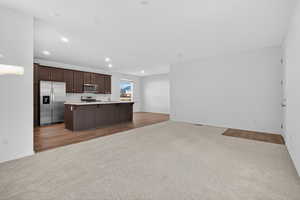 Kitchen with open floor plan, dark colored carpet, dark brown cabinets, stainless steel appliances, and a breakfast bar