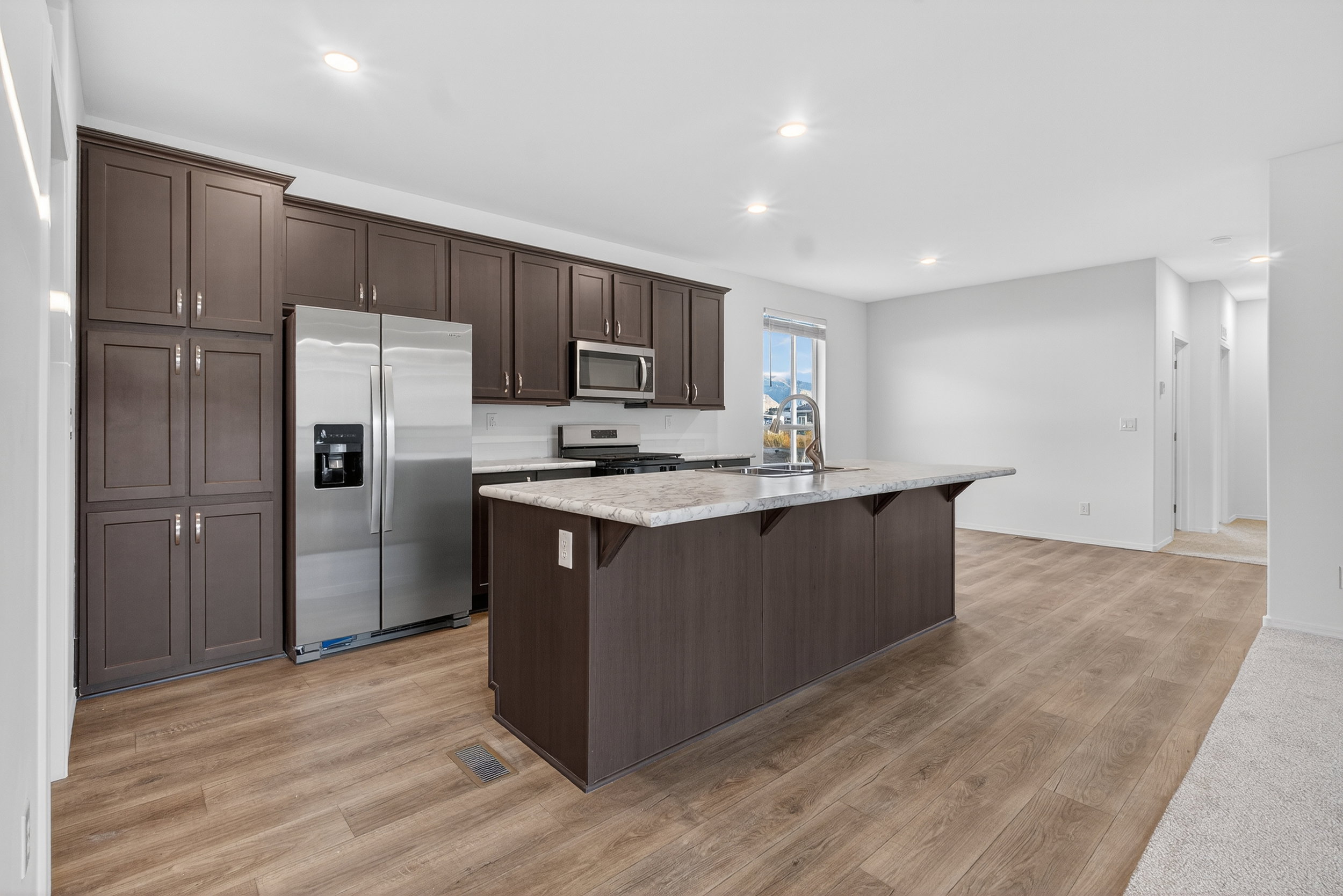 Kitchen with dark brown cabinetry, appliances with stainless steel finishes, light countertops, a kitchen bar, and an island with sink
