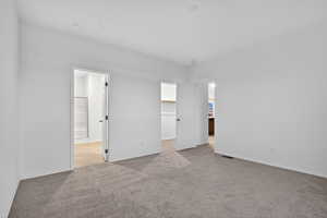 Unfurnished bedroom featuring a walk in closet, light colored carpet, and connected bathroom