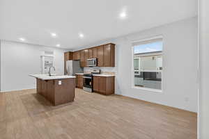 Kitchen featuring light countertops, appliances with stainless steel finishes, a kitchen bar, a center island with sink, and light wood-type flooring