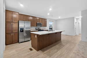 Kitchen featuring stainless steel appliances, a breakfast bar, a center island with sink, light wood-style floors, and recessed lighting