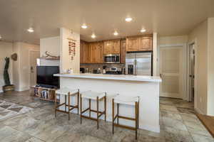 Kitchen with a peninsula, decorative backsplash, stainless steel appliances, a kitchen breakfast bar, and light countertops