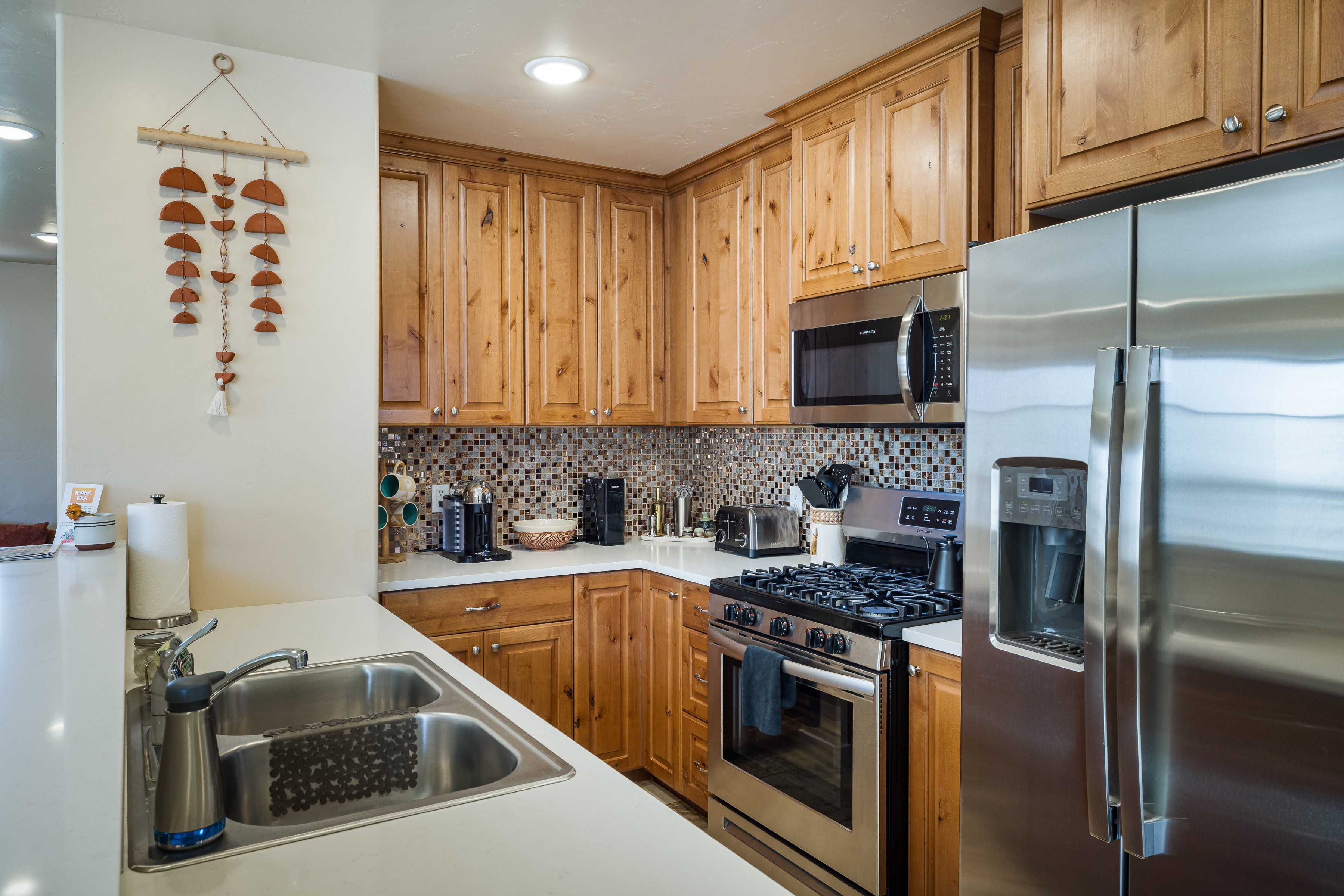 Kitchen with stainless steel appliances, tasteful backsplash, light countertops, and brown cabinetry
