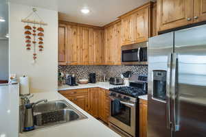 Kitchen with stainless steel appliances, tasteful backsplash, light countertops, and brown cabinetry
