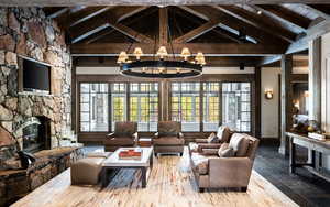 Living room with a stone fireplace, a wood ceiling with exposed beams, stone tile floors, a chandelier, and high vaulted ceiling