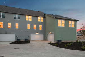 Back of property at dusk featuring stucco siding, driveway, a garage, and a shingled roof