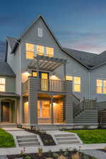 Back of property at dusk featuring a shingled roof, stairs, and a balcony