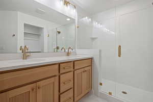 Full bathroom with double vanity, a shower stall, a textured ceiling, and a spacious closet