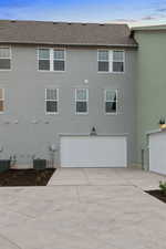Rear view of house with roof with shingles, stucco siding, concrete driveway, and an attached garage