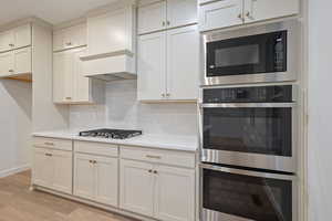 Kitchen with stainless steel appliances, light wood finished floors, tasteful backsplash, white cabinets, and light stone countertops