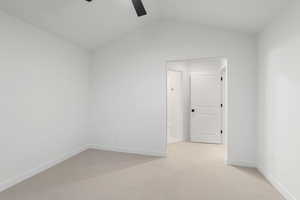 Empty room featuring light colored carpet, lofted ceiling, and a ceiling fan