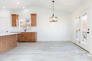 Kitchen with light wood finished floors, pendant lighting, lofted ceiling, brown cabinets, and recessed lighting