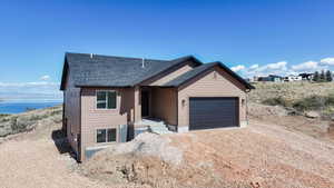 View of front facade featuring dirt driveway, a water view, a garage, and a shingled roof