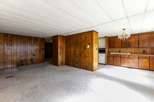 Unfurnished living room featuring light carpet, wood walls, and a chandelier