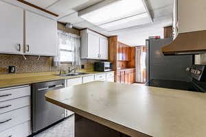 Kitchen with appliances with stainless steel finishes, white cabinetry, under cabinet range hood, light countertops, and decorative backsplash