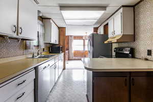Kitchen with wallpapered walls, appliances with stainless steel finishes, light countertops, a chandelier, and white cabinets