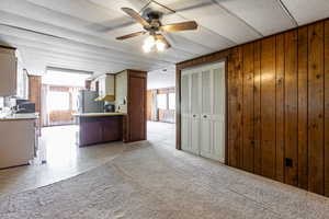Kitchen featuring light countertops, light colored carpet, wood walls, a ceiling fan, and freestanding refrigerator