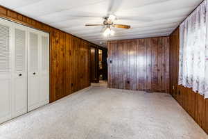 Unfurnished bedroom featuring light carpet, wooden walls, a closet, and a ceiling fan