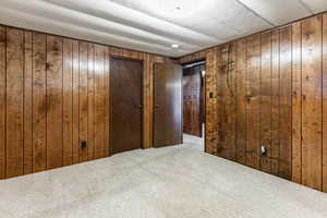 Unfurnished bedroom featuring carpet floors, wooden walls, and a closet
