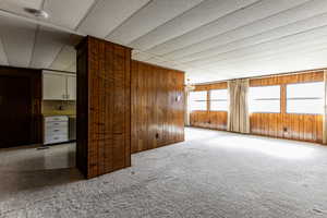 Carpeted spare room with wooden walls, a chandelier, and a smoke detector