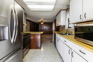 Kitchen featuring appliances with stainless steel finishes, light countertops, a ceiling fan, white cabinetry, and wooden walls