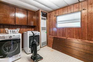Laundry room with wood walls, washing machine and dryer, a heating unit, light flooring, and cabinet space