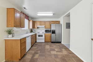 Kitchen with light countertops, appliances with stainless steel finishes, electric panel, brown cabinets, and under cabinet range hood