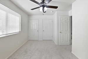 Unfurnished bedroom with light colored carpet, multiple closets, and a ceiling fan