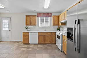 Kitchen with white appliances, light countertops, under cabinet range hood, a textured ceiling, and brown cabinetry