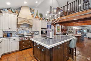 Kitchen featuring hanging light fixtures, dark brown cabinetry, a kitchen island with sink, premium range hood, and tasteful backsplash