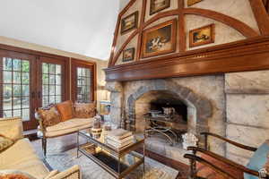 Living room featuring a fireplace with raised hearth, french doors, and vaulted ceiling