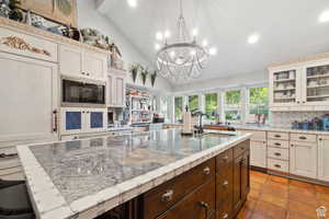 Kitchen featuring vaulted ceiling, tasteful backsplash, a kitchen island with sink, recessed lighting, and built in microwave
