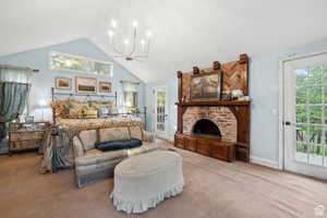 Carpeted bedroom with access to outside, high vaulted ceiling, a chandelier, and a fireplace