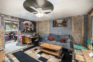 Carpeted living room with wooden walls, a ceiling fan, and wallpapered walls