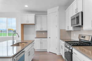 Kitchen with stainless steel appliances, white cabinetry, light wood-type flooring, and recessed lighting