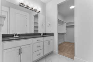 Bathroom featuring double vanity, a spacious closet, light marble finish floors, and light carpet