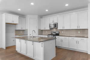Kitchen featuring tasteful backsplash, white cabinets, a center island with sink, and recessed lighting