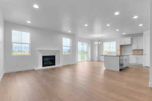 Unfurnished living room with recessed lighting, a glass covered fireplace, a chandelier, and light wood-style floors