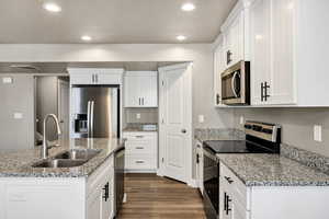 Kitchen featuring appliances with stainless steel finishes, white cabinets, light stone counters, recessed lighting, and dark wood-style flooring
