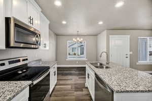 Kitchen featuring stainless steel appliances, white cabinets, light stone countertops, dark wood-style floors, and recessed lighting