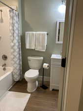 Full bathroom featuring shower / tub combo with curtain, dark wood-style floors, and vanity