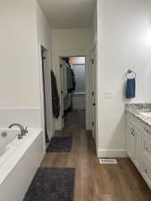 Full bathroom with a walk in closet, dark wood finished floors, vanity, a garden tub, and a shower stall