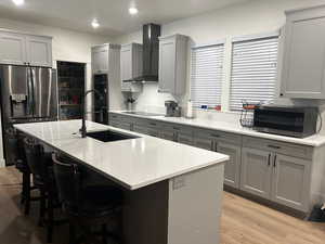Kitchen with gray cabinetry, black appliances, light wood-style floors, wall chimney range hood, and a kitchen breakfast bar