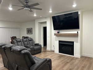Living room with light wood-style flooring, a fireplace, ceiling fan, and recessed lighting
