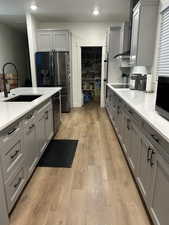 Kitchen featuring gray cabinetry, light stone countertops, refrigerator with ice dispenser, light wood-style floors, and black electric stovetop