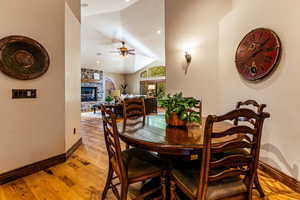 Dining space with lofted ceiling, light wood-style flooring, a fireplace, ceiling fan, and recessed lighting