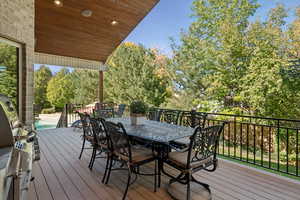 Deck with area for grilling, outdoor dining space, view of scattered trees, and an outdoor pool