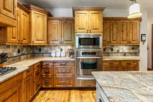 Kitchen featuring decorative backsplash, stainless steel appliances, light stone countertops, and brown cabinets