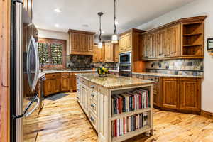 Kitchen featuring open shelves, brown cabinetry, light stone countertops, backsplash, and appliances with stainless steel finishes