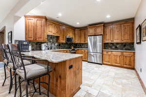 Kitchen featuring brown cabinets, a breakfast bar, a peninsula, appliances with stainless steel finishes, and recessed lighting